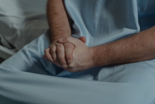person in hospital gown with clasped hands