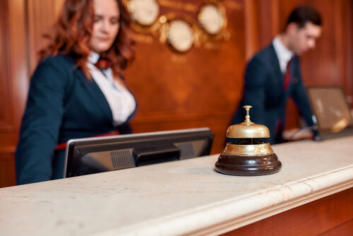 Attractive executives at the reception desk of a hotel in the background. Focus on a service bell. Horizontal shot